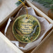 A circular ornament with a natural landscape design, featuring a waterfall, trees, and flowers, is displayed in a box.