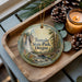 A wooden tray with a decorative ornament featuring a scenic image of a waterfall and pine trees, along with pine cones and a lit candle.