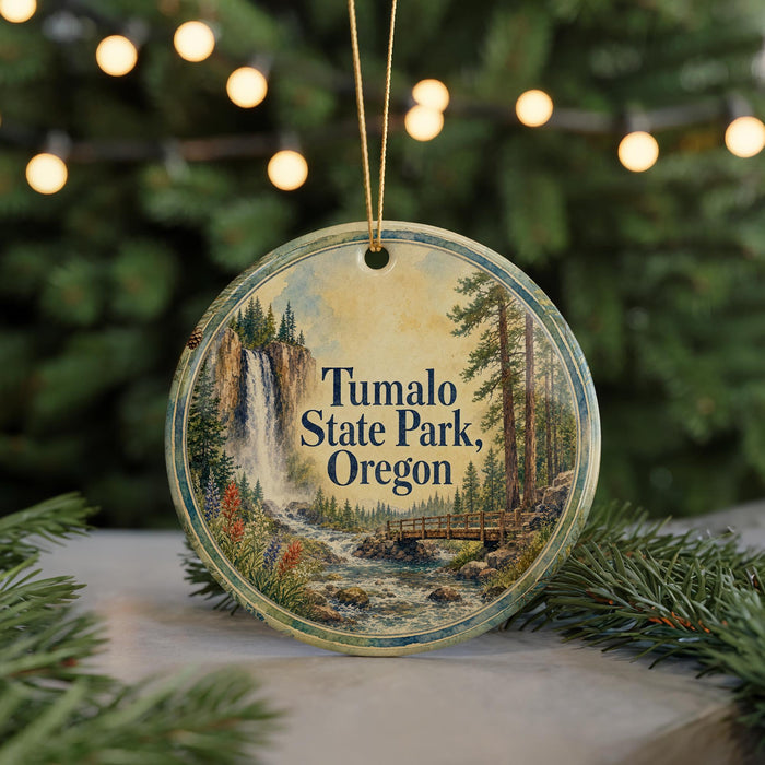 A circular ornament with a painting of a waterfall and forest, hanging on a string.