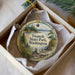 A decorative ornament in a box, featuring a scenic landscape with pine trees, a lake, and mountains.