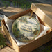 A circular ornament with a scenic landscape of Twanoh State Park, Washington, displayed in a wooden box with a gold string.