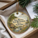 A decorative ornament with a scenic landscape of a river, waterfall, and a house, hanging from a string.