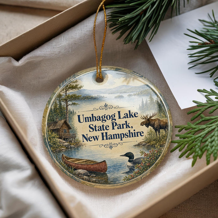 A decorative ornament with a scenic image of Umbog Lake State Park, New Hampshire, featuring a moose, a canoe, and a bird.