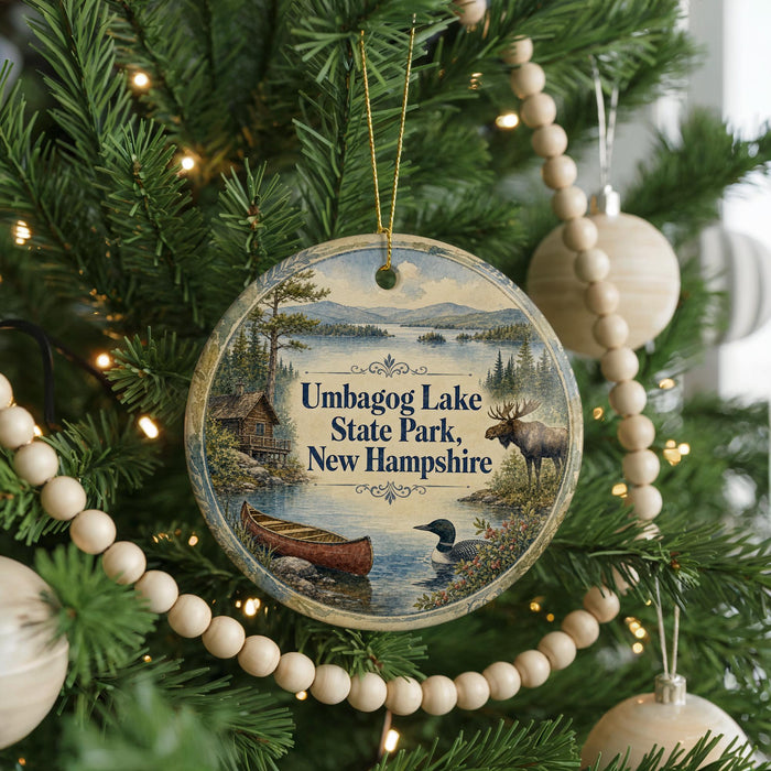 A round ornament hanging on a Christmas tree, featuring a scenic image of Umbog Lake, State Park, and New Hampshire.