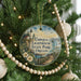 A round ornament hanging on a Christmas tree, featuring a lighthouse and a scenic landscape.