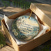 A decorative ornament in a box, featuring a lighthouse and a scenic landscape, with the text "Umpqua Lighthouse State Park, Oregon" printed on it.