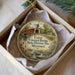 A decorative ornament in a white box, featuring a painting of a covered bridge and a scenic landscape.