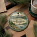 A round ornament with a scenic landscape of a lake, mountains, and pine trees, along with a bird and a canoe, is displayed on a wooden surface.