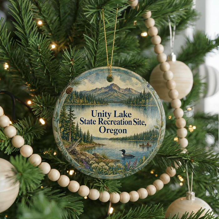 A round ornament hanging on a Christmas tree, featuring a scenic landscape with mountains, a lake, and pine trees.