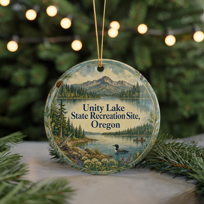 A round ornament with a scenic landscape featuring a lake, mountains, and pine trees, along with a bird in the water.