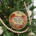 A round ornament hanging on a Christmas tree, featuring a desert landscape with mountains and a bird in flight.