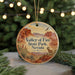 A round ornament with a desert landscape and a mountain range, featuring a bird and a plant, is displayed in front of a blurred background with Christmas lights.