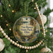 A round ornament hanging on a Christmas tree, featuring a scenic landscape with a bridge and a lake.