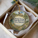A decorative ornament in a box, featuring a scenic landscape with a house, trees, and a waterfall.