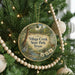 A round ornament hanging on a Christmas tree, featuring a scenic image of a park with a river and trees.