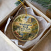 A decorative ornament in a box, featuring a scenic landscape with a river, bridge, and mountains.