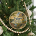 A round ornament hanging on a Christmas tree, featuring a scenic landscape with a bridge and mountains in the background.