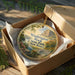 A decorative ornament in a box, featuring a scenic landscape with a bridge and trees, with the text "Washington Rock State Park New Jersey" printed on it.