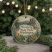 A circular ornament with a scenic landscape of Wenberg State Park, Washington, featuring a waterfall and pine trees, is displayed on a table with Christmas lights in the background.