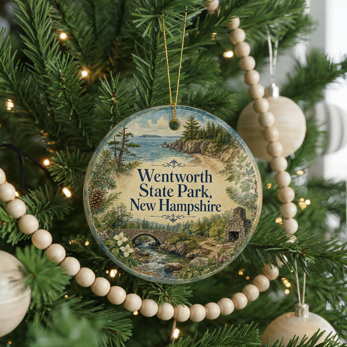 A round ornament hanging on a Christmas tree, featuring a scenic landscape with a bridge and a river.