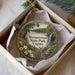A decorative ornament in a box, featuring a scenic landscape with a deer, trees, and a waterfall.