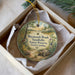 A round ornament with a nature scene, featuring a bird, a turtle, and a forest landscape, is displayed in a box.