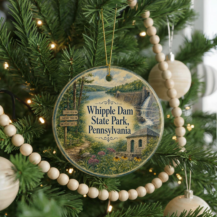 A round ornament hanging on a Christmas tree, featuring a scenic image of Whipple Dam State Park, Pennsylvania.
