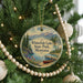 A round ornament hanging on a Christmas tree, featuring a scenic landscape with mountains, pine trees, and a lake.