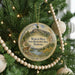 A round ornament on a Christmas tree, featuring a scenic landscape with mountains, trees, and a cat.