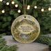 A round ornament with a landscape scene featuring a mountain, pine trees, and a cat, hanging from a string.