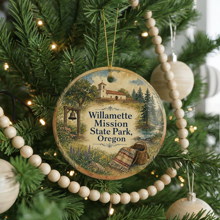 A Christmas tree ornament featuring a scenic image of Willamette Mission State Park, Oregon, with a bell and a basket of blankets.