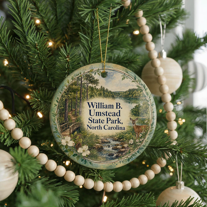 A round ornament hanging on a Christmas tree, featuring a scenic image of William B. Umstead State Park in North Carolina.