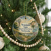 A round ornament hanging on a Christmas tree, featuring a scenic landscape with a windmill, a path, and a body of water.