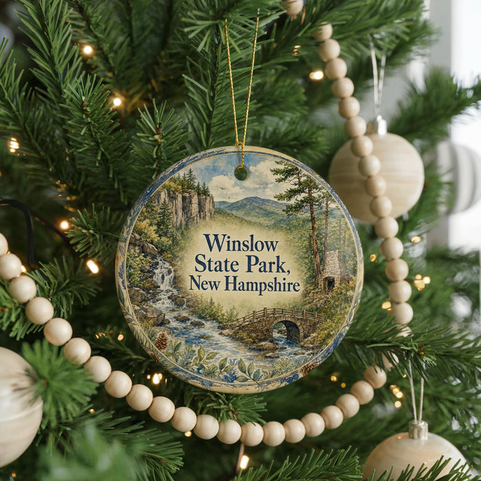 A round ornament hanging on a Christmas tree, featuring a scenic landscape with a waterfall and a bridge.
