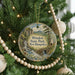 A round ornament hanging on a Christmas tree, featuring a scenic landscape with a waterfall and a bridge.