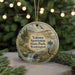 A circular ornament with a scenic landscape featuring a waterfall, pine trees, and wildlife, including a pheasant, is displayed in front of a blurred background with Christmas lights.