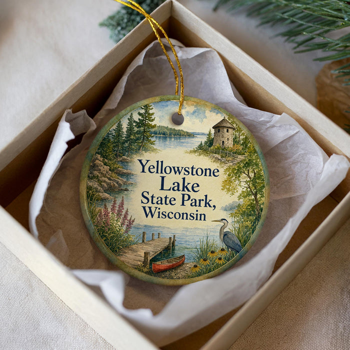 A decorative ornament in a white box, featuring a scenic landscape with a lake, a small building, and a bird.