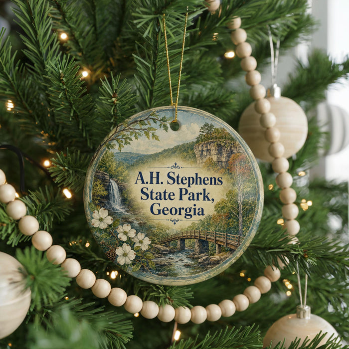 A round ornament hanging on a Christmas tree, featuring a scenic landscape with a waterfall and a bridge.