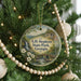 A round ornament hanging on a Christmas tree, featuring a scenic landscape with a waterfall and a bridge.
