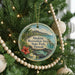 A round ornament hanging on a Christmas tree, featuring a tropical landscape with palm trees, a beach, and a mountain range.