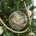 A round ornament on a Christmas tree, featuring a scenic landscape with a lighthouse and a river, with the text "Albert E. Sleeper State Park, Michigan" displayed on it.