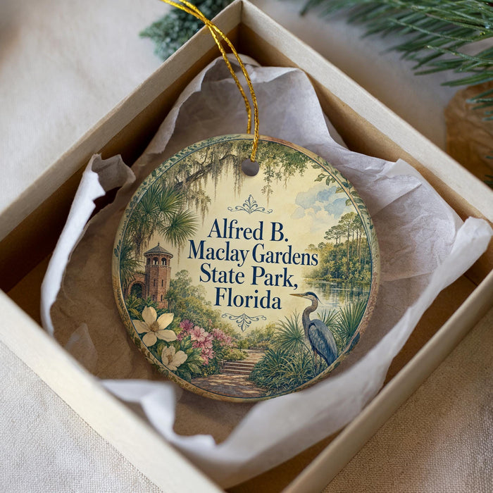 A round ornament with a tropical garden scene, featuring a bird, flowers, and a tower, is displayed in a box.