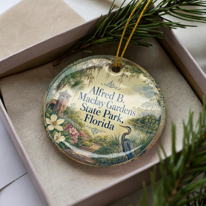 A decorative ornament in a box, featuring a scenic landscape with a bird, palm trees, and a building, along with the text "Alfred B Maclay Gardens State Park, Florida".