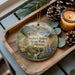 A wooden tray with a decorative ornament featuring a scenic landscape of Andrew Molera State Park, California, and pine cones.