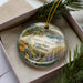A decorative ornament in a box, featuring a scenic landscape with mountains, trees, and flowers, along with the text "Andrew Moles State Park, California".