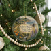 A round ornament hanging on a Christmas tree, featuring a scenic landscape of mountains, trees, and a river.
