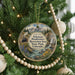 A Christmas ornament hanging on a tree, featuring a scenic landscape with mountains, a river, and a train.