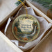 A decorative ornament in a box, featuring a scenic landscape with a waterfall and pine trees.