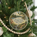 A circular ornament hanging on a Christmas tree, featuring a scenic landscape with a lake and trees.