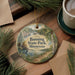 A decorative ornament with a scenic landscape of Banning State Park, Minnesota, featuring a lake, forest, and waterfall. The ornament is hanging on a wooden surface, surrounded by pine branches and a cup of coffee.